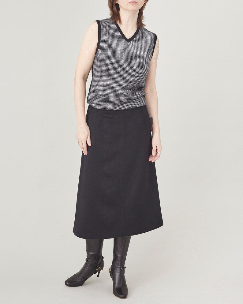 Person wearing a sleeveless patterned top and black skirt on a plain background