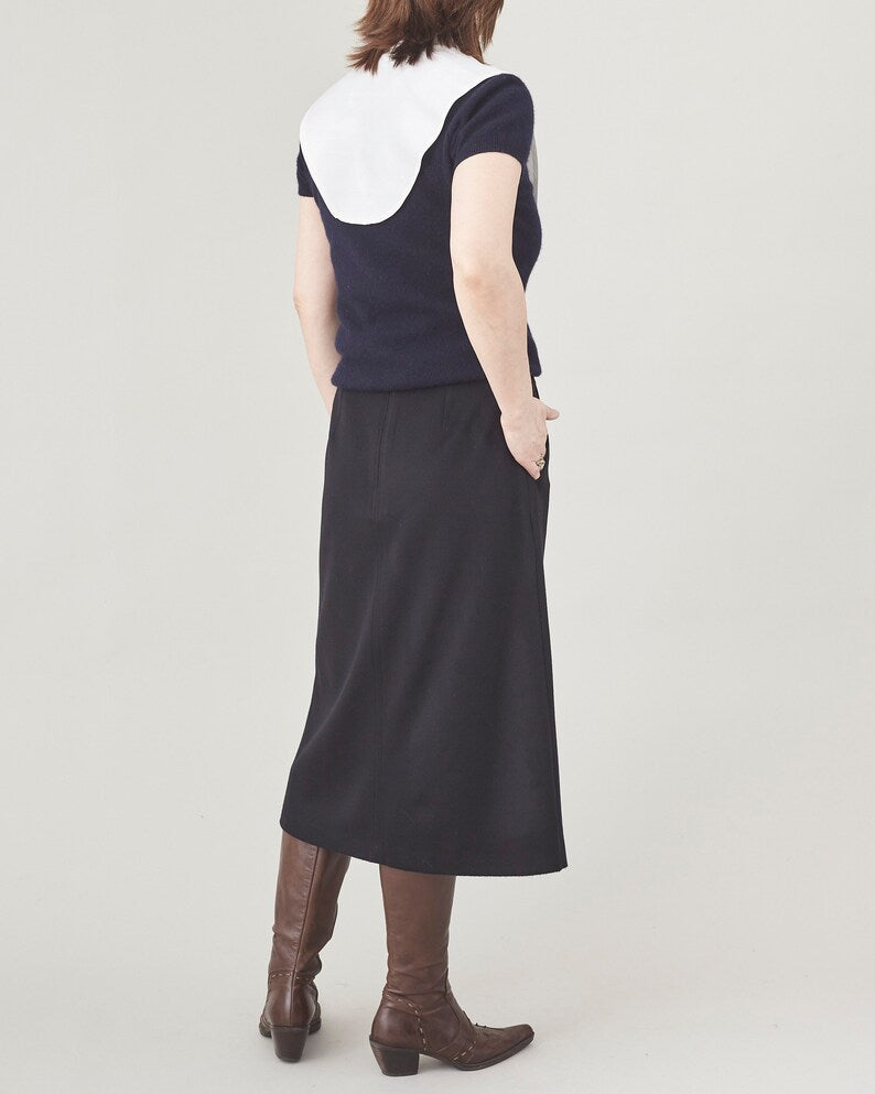 Person wearing a navy sweater with a white collar, black midi skirt and brown boots on a plain background