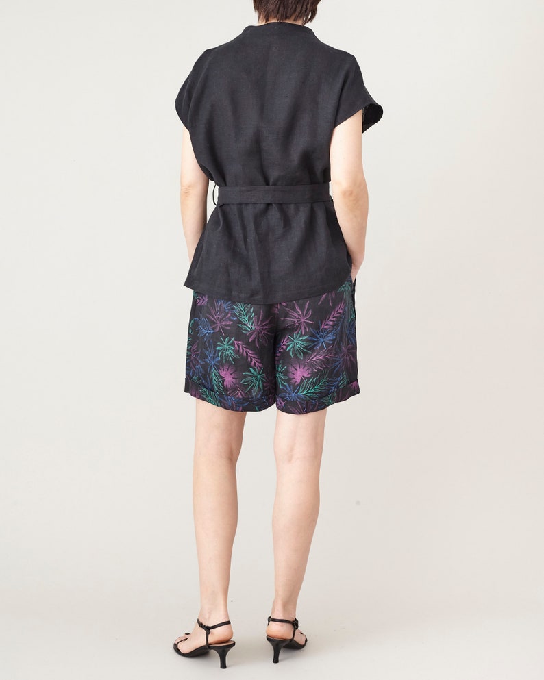 Person wearing a black outfit with colorful leaf patterned shorts on a white background