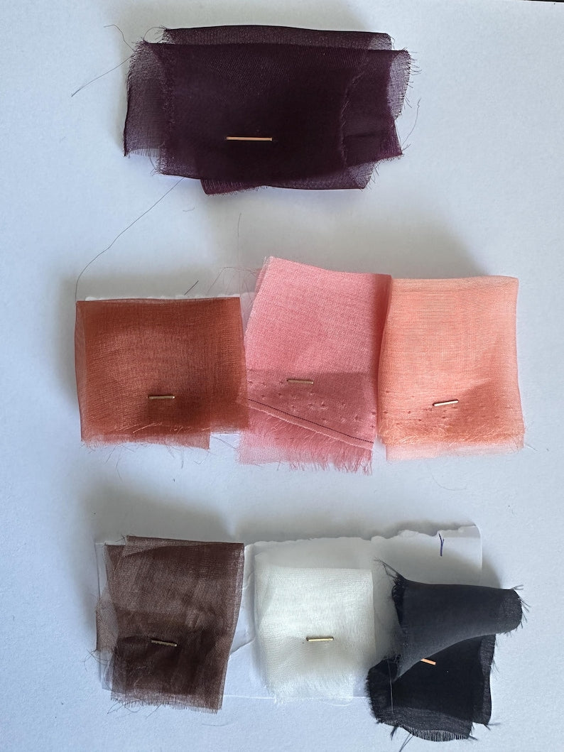 Color swatches of sheer silk organza fabric in purple, terracotta, pink, peach, brown, white, and black pinned on white paper
