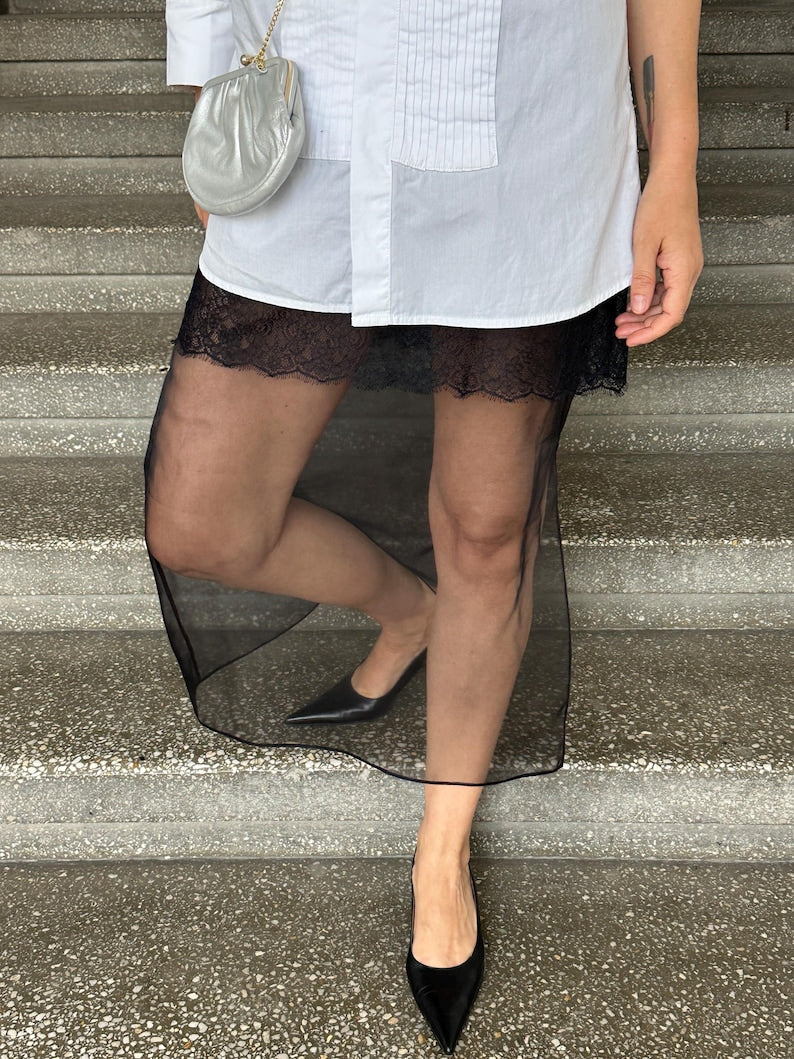 Sheer black silk organza skirt layered over black lace slip, styled with a long white shirt and pointed black heels