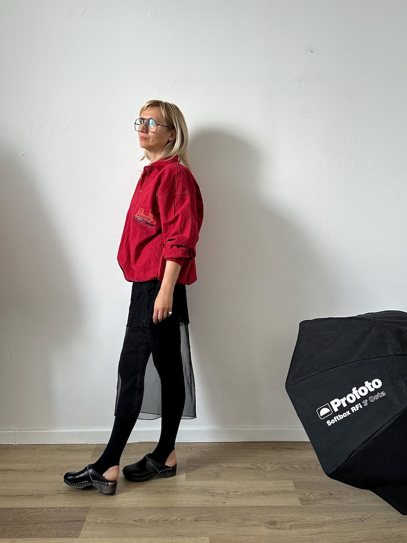 Person wearing a red jacket standing next to a ProFoto photography light modifier against a white wall.