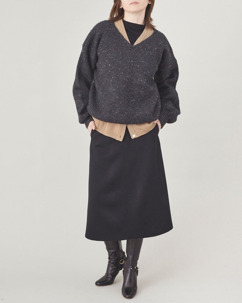 Person wearing a dark gray sweater over a beige shirt with a black skirt on a white background
