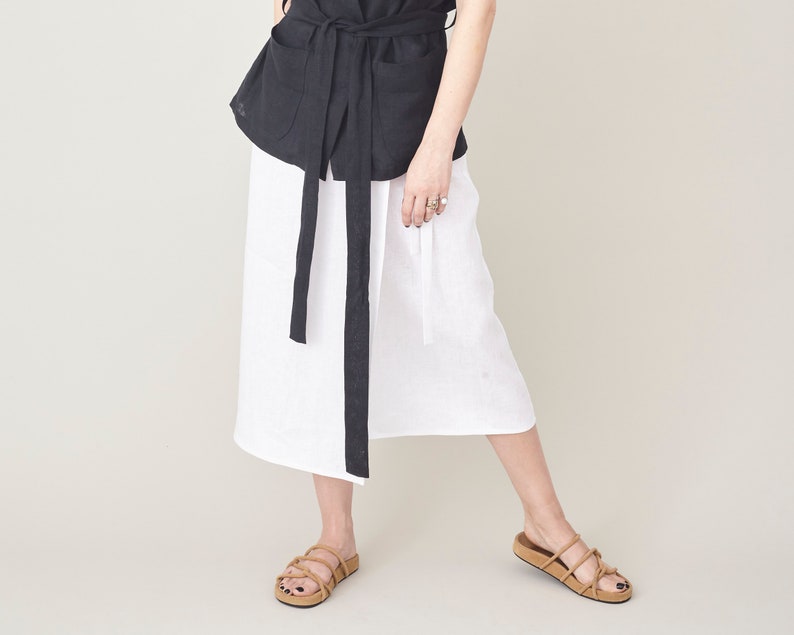 Person wearing a black top and white skirt with a belt on a plain background
