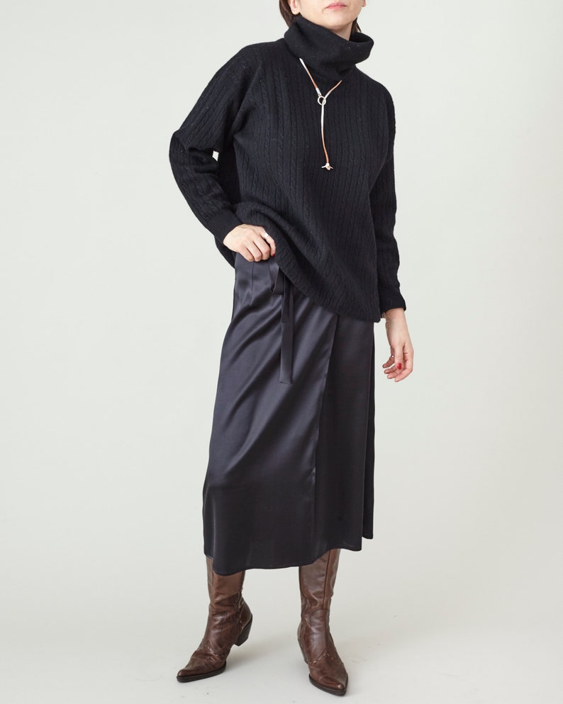 Person wearing a black ribbed sweater and dark skirt with brown boots on a white background