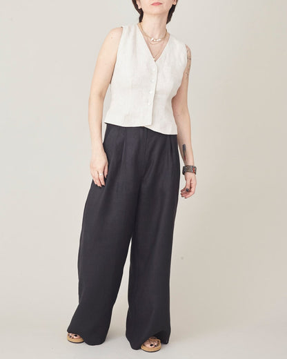Person wearing a beige sleeveless top and black wide-leg pants on a plain background