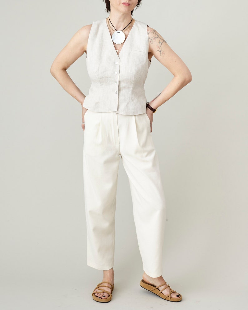 Person wearing a beige sleeveless top and white pants with a plain background