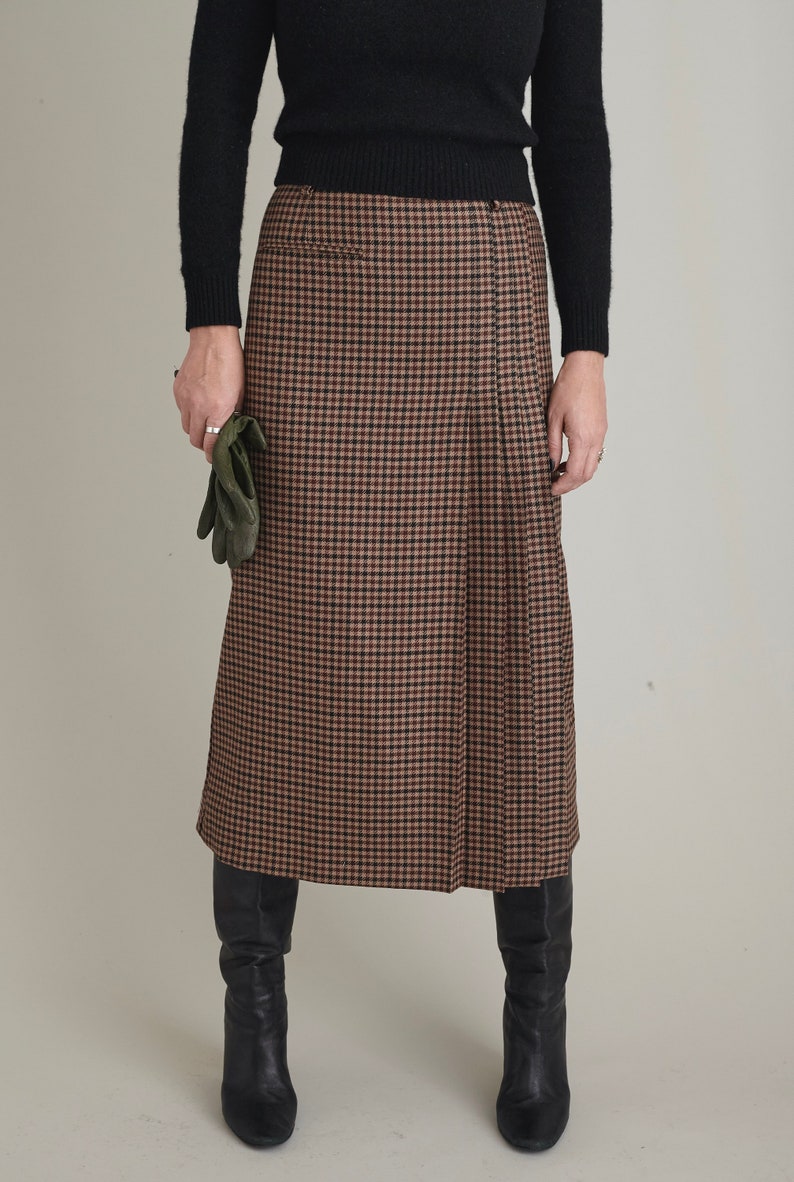 Person wearing a brown checkered skirt with a black top and boots on a plain background
