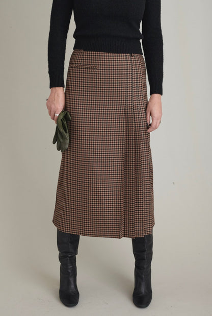 Person wearing a brown checkered skirt with a black top and boots on a plain background