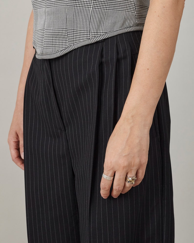 Person wearing black pinstripe pants and a checkered top on a neutral background
