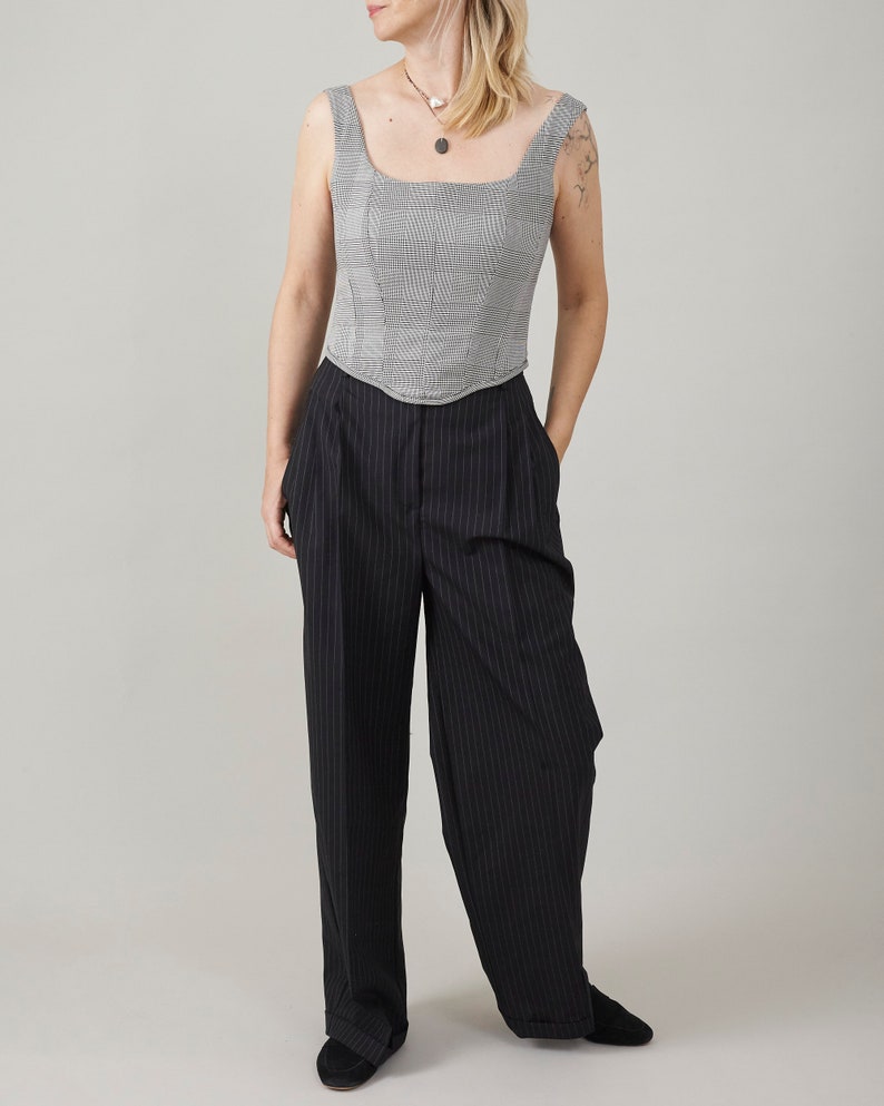Woman wearing a sleeveless checkered top and black pinstripe pants on a plain background