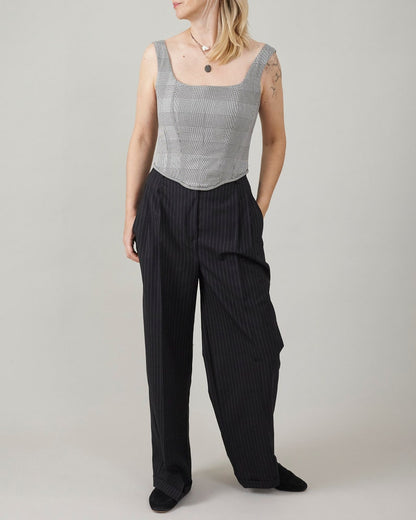 Woman wearing a sleeveless checkered top and black pinstripe pants on a plain background