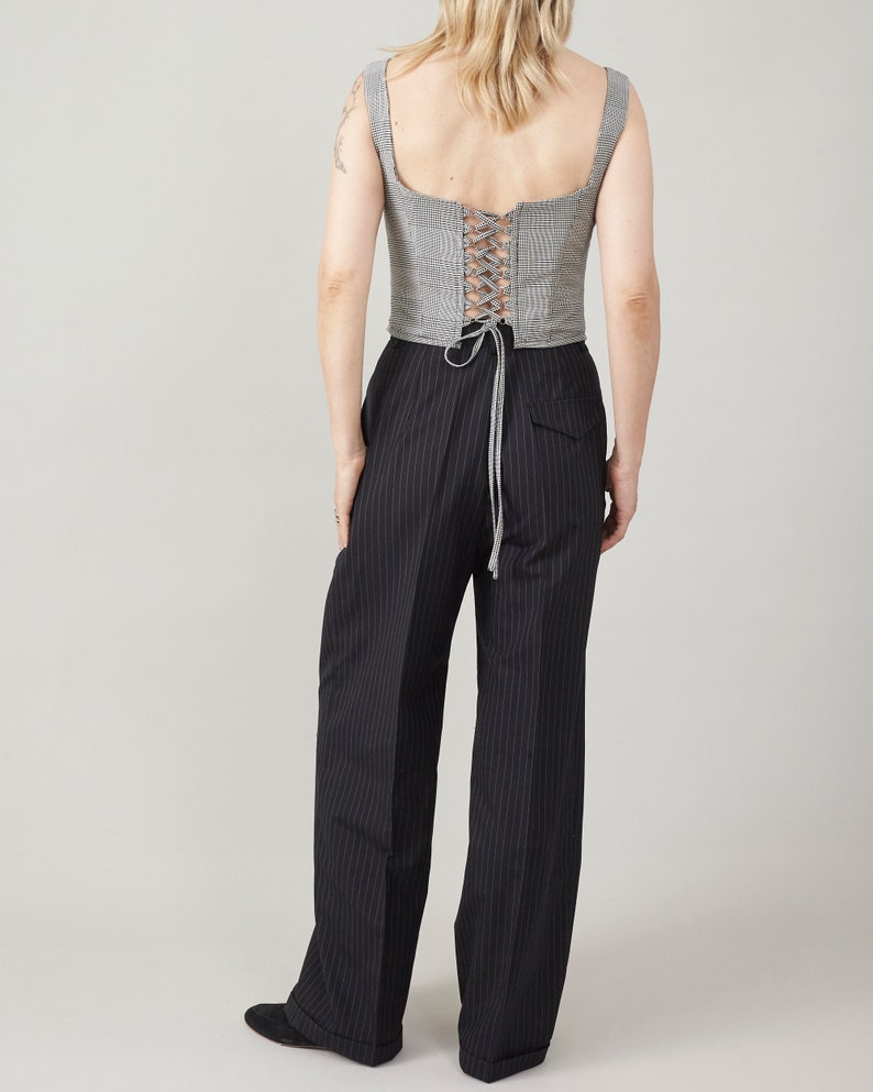 Person wearing a checkered top with lace-up, open back and black pinstripe pants on a plain background