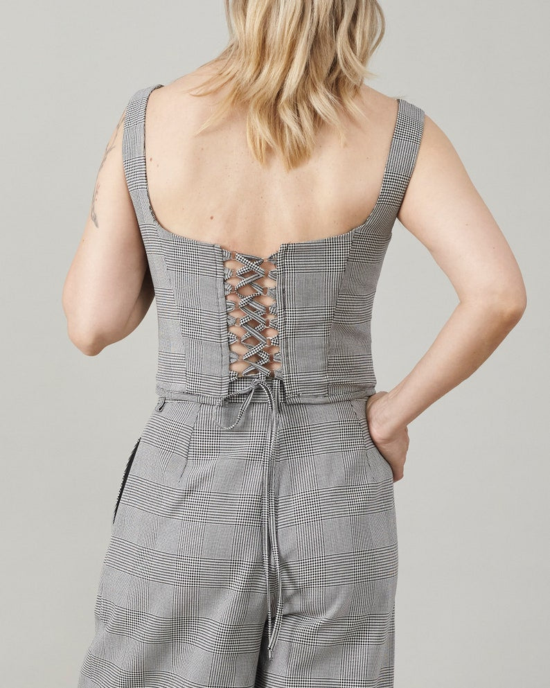 Person wearing a gray checkered bustier top with a lace-up back on a plain background