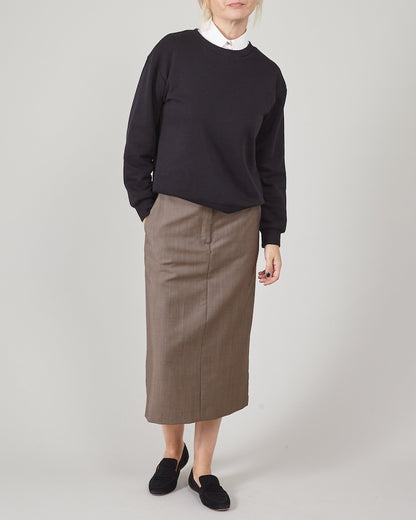 Person wearing a black sweatshirt, brown skirt and black loafers on a plain background