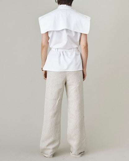 Person wearing a white sleeveless top with oversized cape collar and beige pants on a plain background