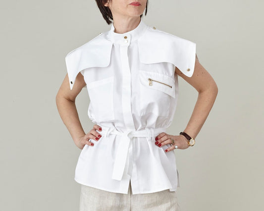 Woman wearing a white sleeveless shirt with a tie waist against a plain background