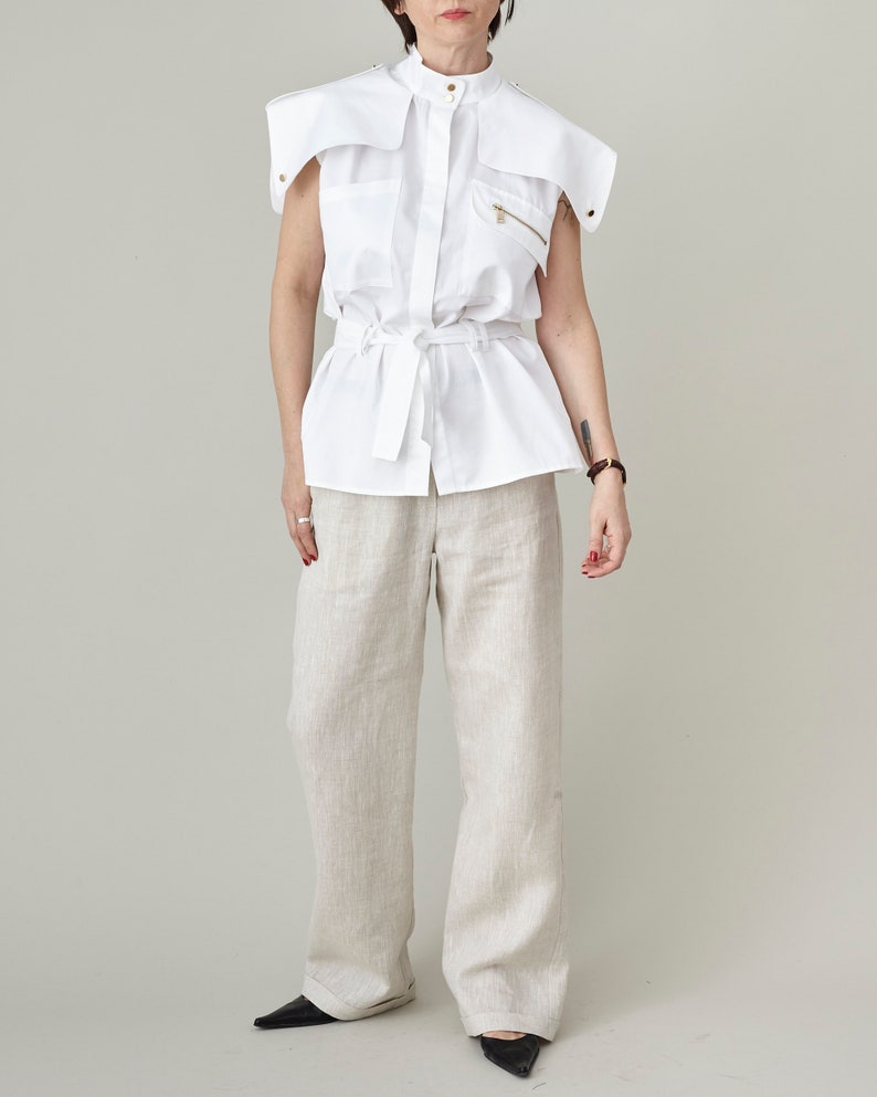 Person wearing a white sleeveless blouse and light-colored pants on a plain background
