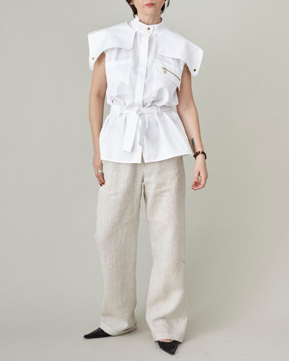 Person wearing a white sleeveless blouse and light-colored pants on a plain background