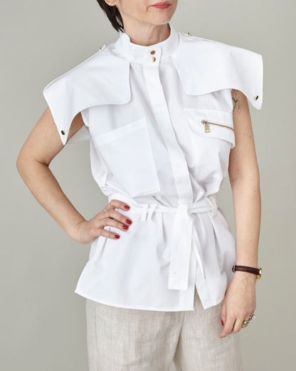 Person wearing a white sleeveless top with a belt against a neutral background