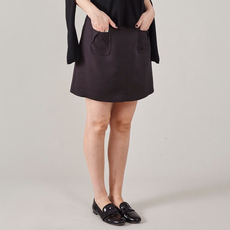 Person wearing a dark brown skirt with pocket details on a plain background