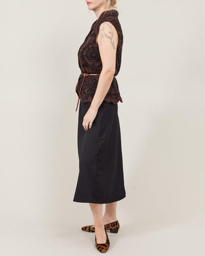 Woman wearing a patterned top and black skirt with leopard print shoes on a plain background