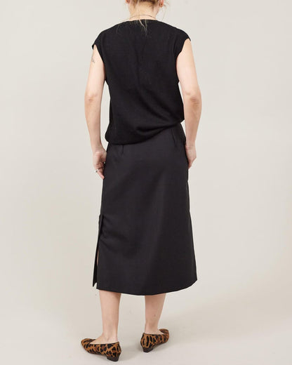 Person wearing a black sleeveless top and skirt set on a plain background