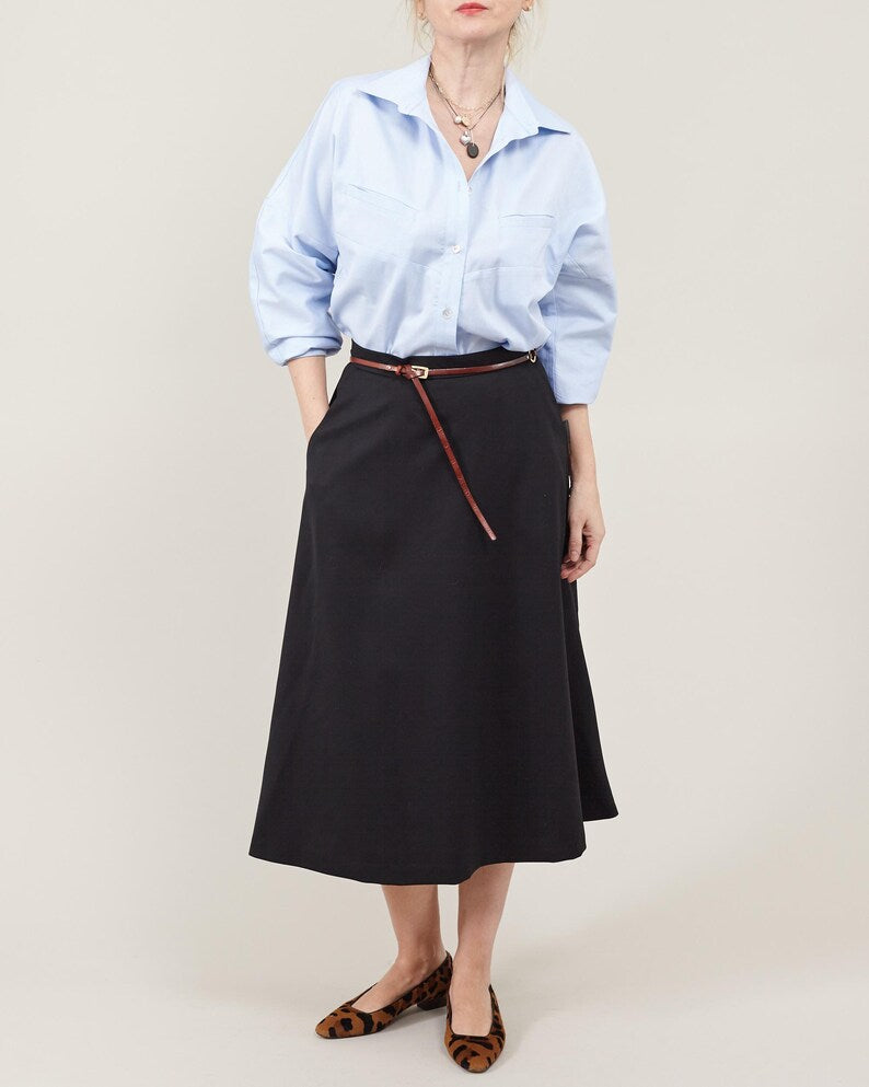 Person wearing a light blue shirt and black skirt with a brown belt on a beige background