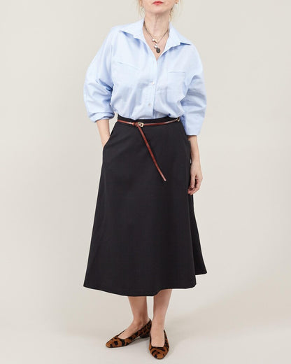 Person wearing a light blue shirt and black skirt with a brown belt on a beige background