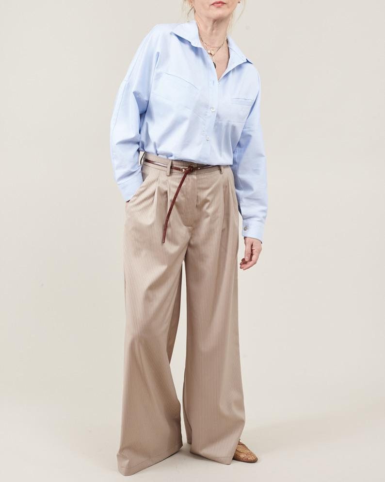 Person wearing a light blue shirt and beige pants on a plain background