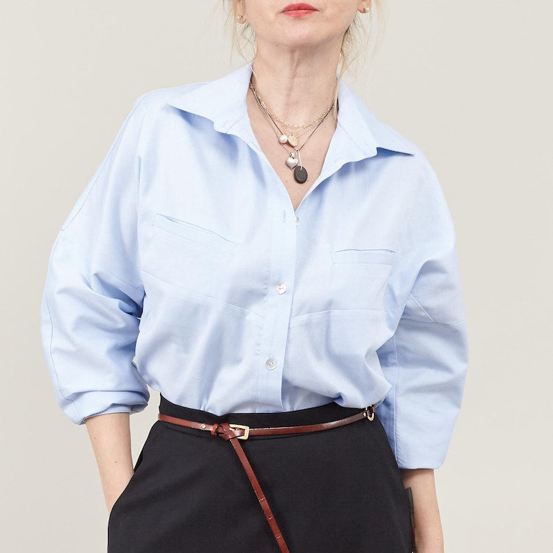 Person wearing a light blue shirt and black skirt with brown belt with a neutral background