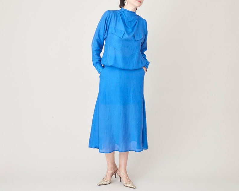 Full front view of a blue silk midi dress with long sleeves, gathered neckline and flowing skirt.
