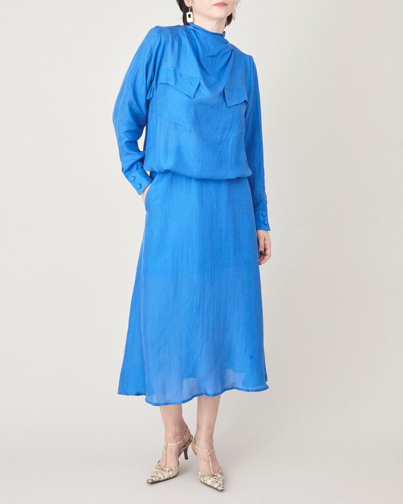 Blue silk midi dress with a tie waist, long sleeves and flowing mid-calf skirt.
