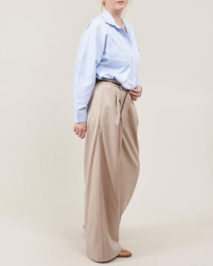 Person wearing a light blue shirt and beige wide-leg pants on a beige background