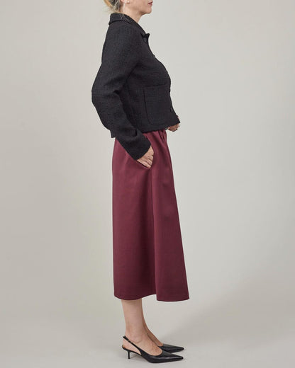 Person wearing a black jacket and burgundy skirt on a plain background