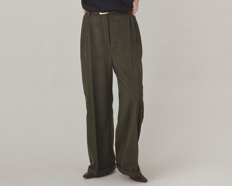 Front view of olive cashmere wide-leg pants with a high pleated waist and pressed creases, worn with a black top.
