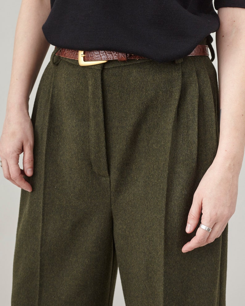 Close-up of the high pleated waist and front closure on olive cashmere wide-leg pants.