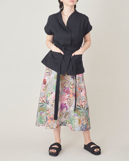 Person wearing a black top and colorful floral skirt on a plain background