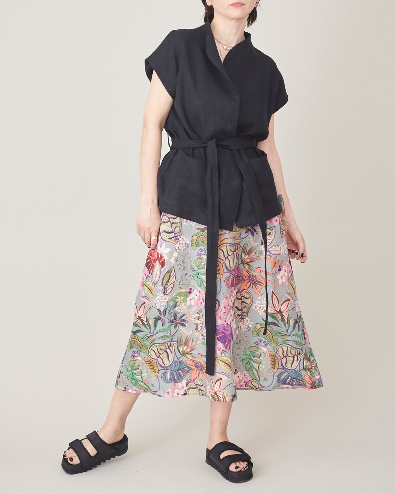 Person wearing a black sleeveless top and colorful floral skirt on a plain background