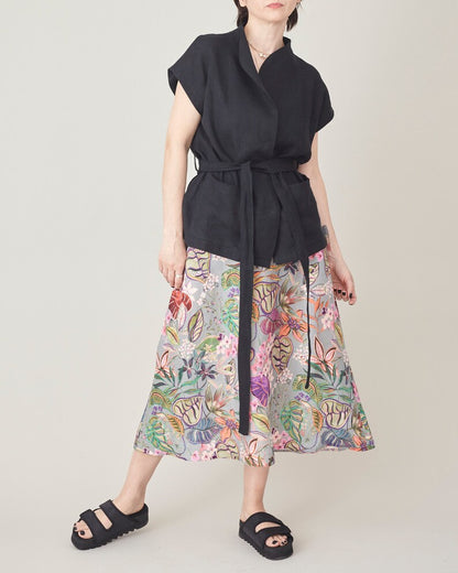 Person wearing a black sleeveless top and colorful floral skirt on a plain background