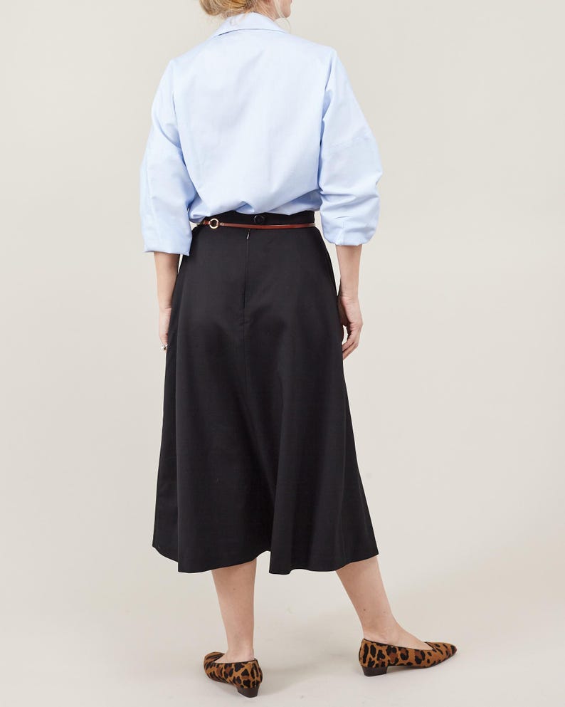 Person wearing a light blue shirt and black skirt on a beige background