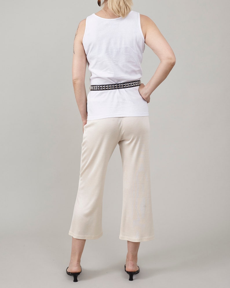 Back view of Fine Thee ivory cropped silk jersey pants, styled with a white tank top, a studded black belt, and low-heeled black mules.