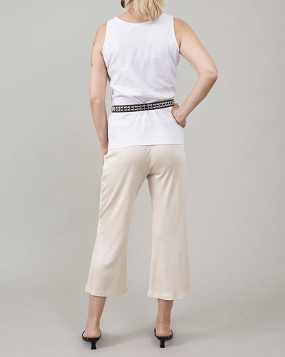 Back view of Fine Thee ivory cropped silk jersey pants, styled with a white tank top, a studded black belt, and low-heeled black mules.