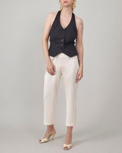 Full-length view of Fine Thee ivory cropped silk jersey pants styled with a tailored black pinstripe halter vest and cream mule heels, elegant minimalist look.
