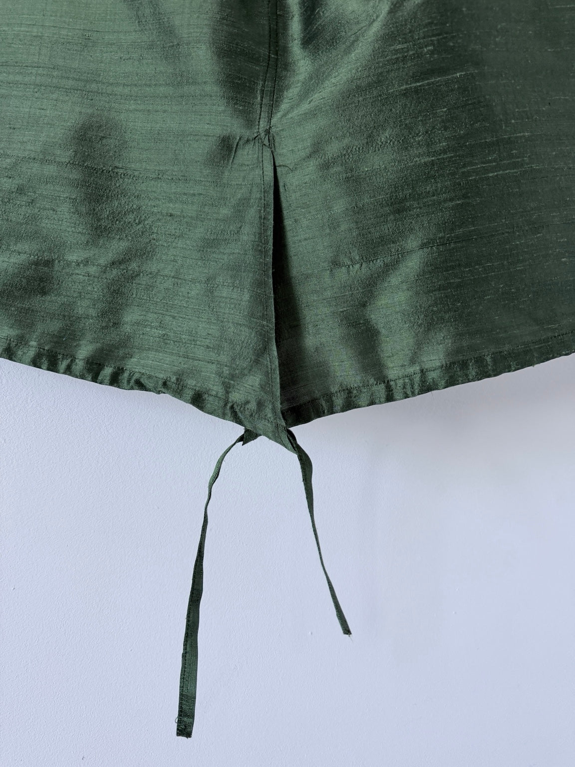Close up of green silk skirt overlapping front slit and adjustable hem