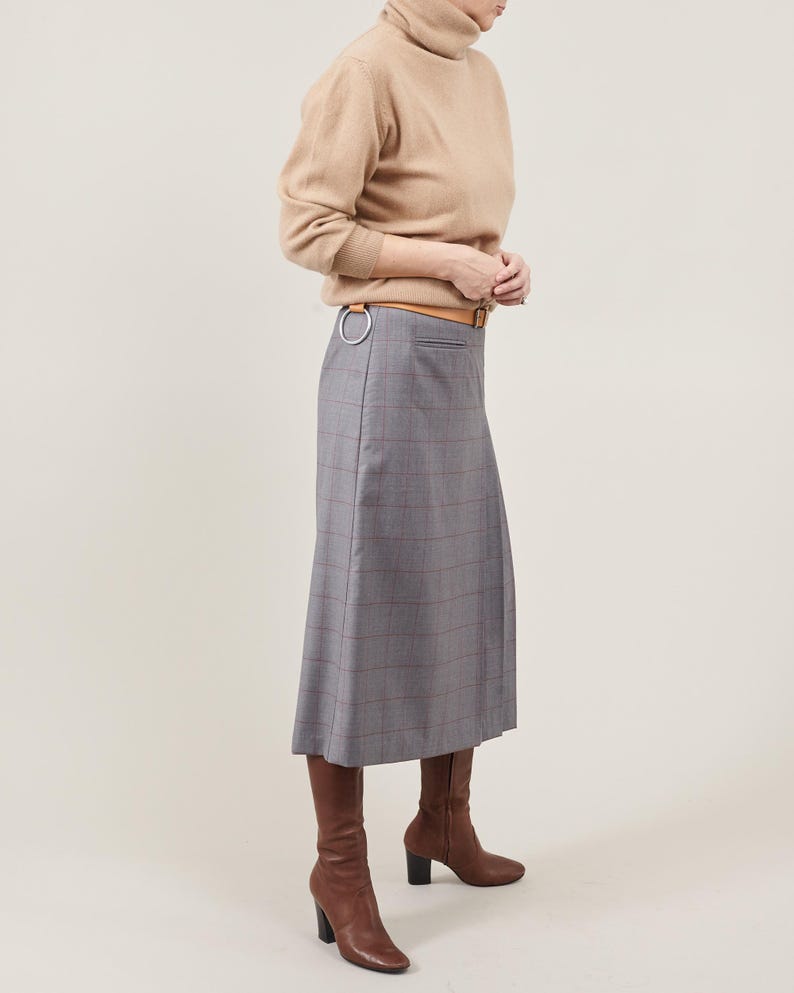 Person wearing a beige sweater, gray checkered skirt, and brown boots on a plain background