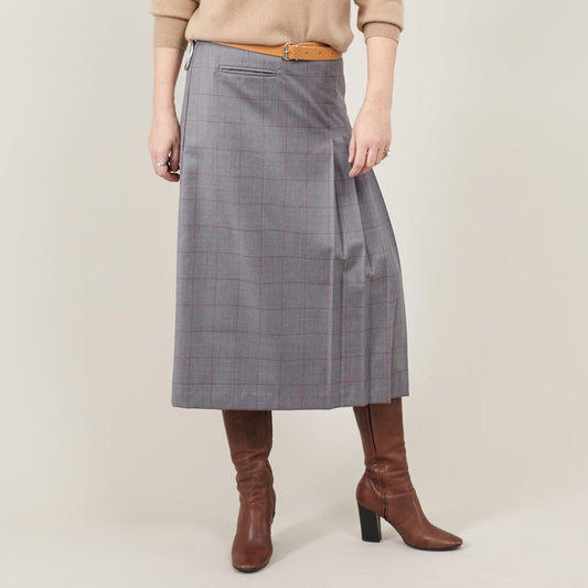 Person wearing a gray plaid skirt with brown boots on a beige background