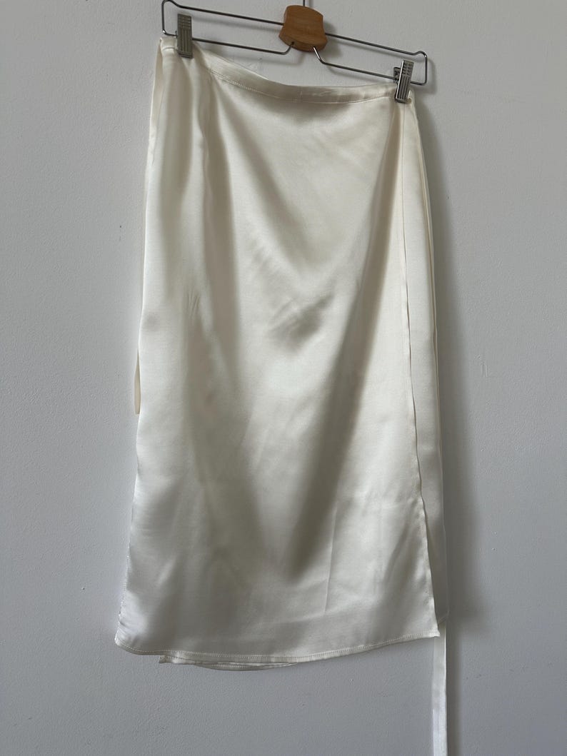 White satin silk skirt hanging on a rack against a plain wall