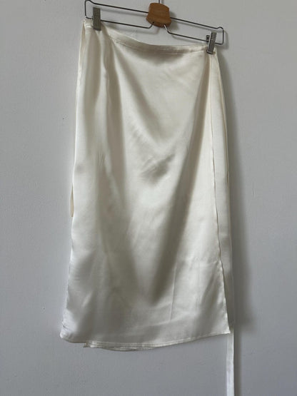 White satin silk skirt hanging on a rack against a plain wall