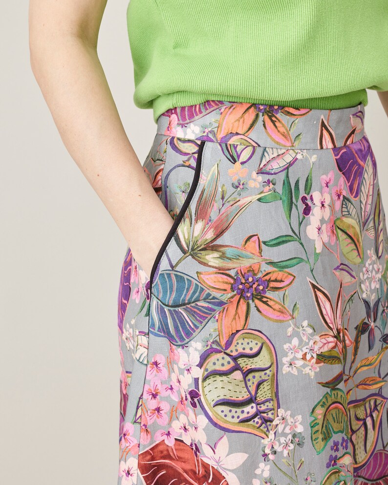 Person wearing a green top and colorful floral skirt on a plain background